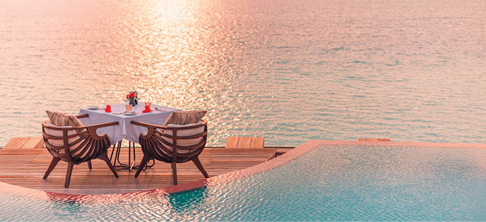 Seascape view under sunset light with dining table with infinity pool around  Romantic tropical getaway for two, couple concept  Chairs, food and romance  Luxury destination dining, honeymoon template