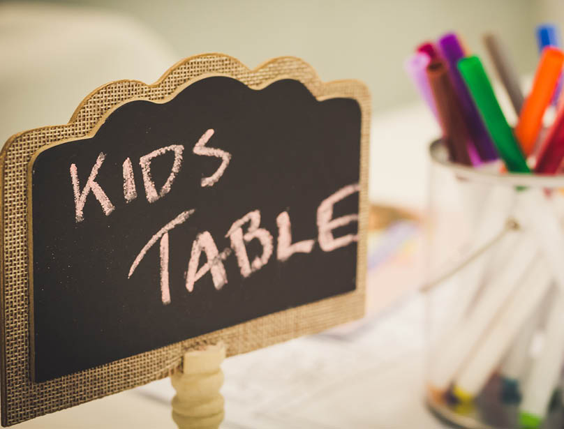 Kids entertainment table at a wedding with colorful markers in a jar and a chalkboard sign