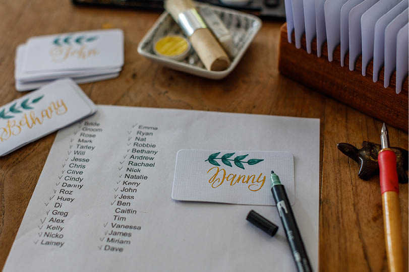 Wedding calligraphy - guest list and handwritten place cards with names  Golden writing with green flourish on white paper  Gold paint, nib pen, card holder 