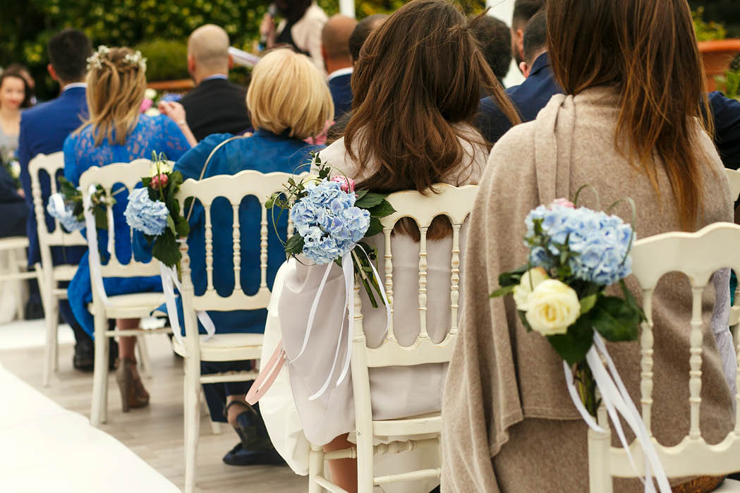 Look from behind on guests sitting on white chairs during the ceremony