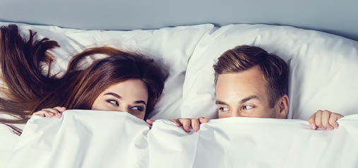 Young attractive playfull couple peeping from bedsheet on the bed at bedroom  Caucasian models in love, relationship, dating, happy people, bedtime concept shot  Horizontal banner composition 
