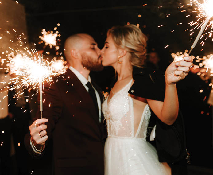 at the wedding, the bride and groom hold sparklers in their hands, and friends and relatives stand in the background