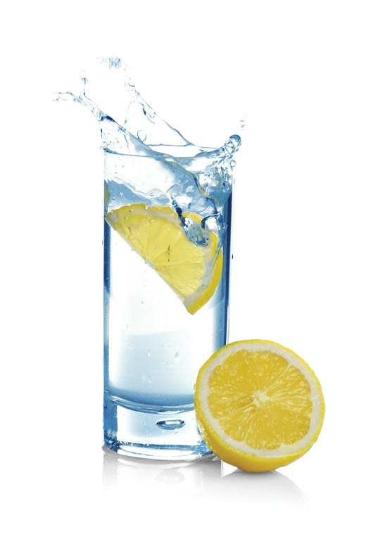 Falling lemon slice into glass with water on white background