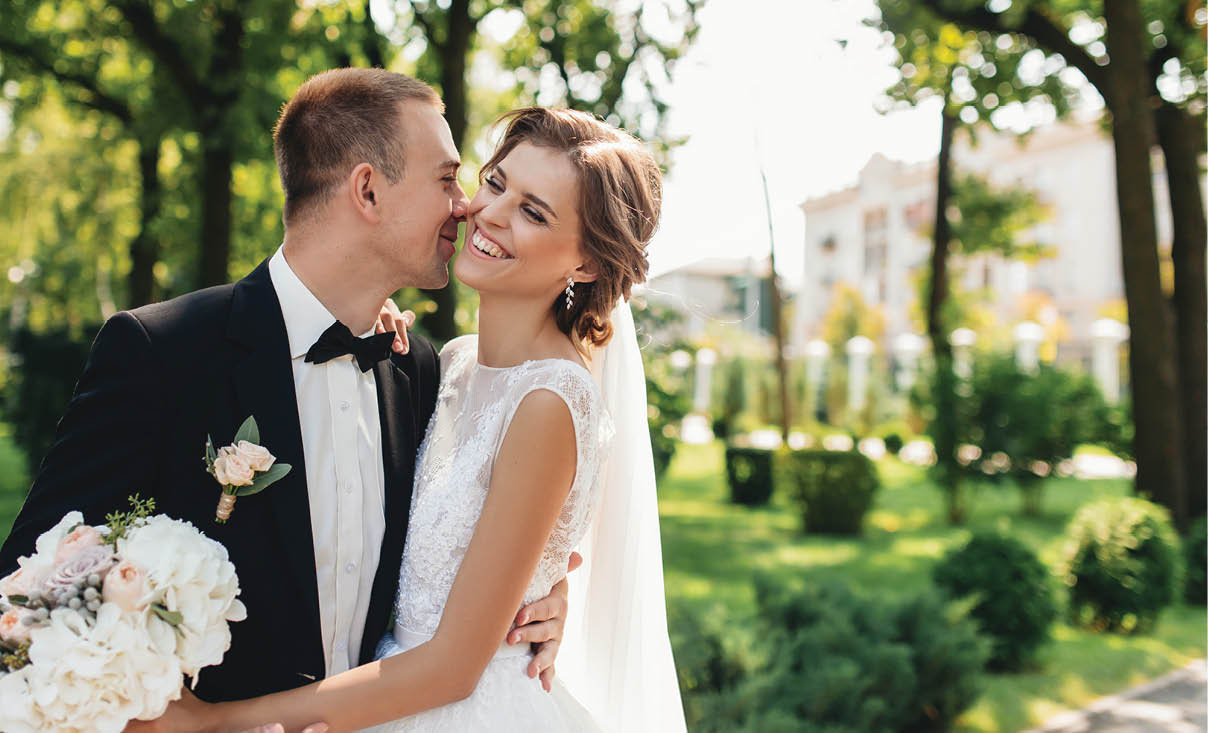 Groom hugging his laughing bride in green park