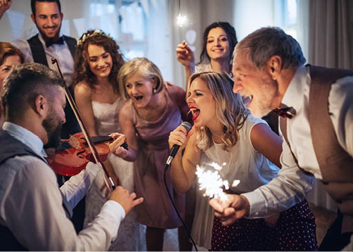 A young bride, groom and other guests dancing and singing on a wedding reception.