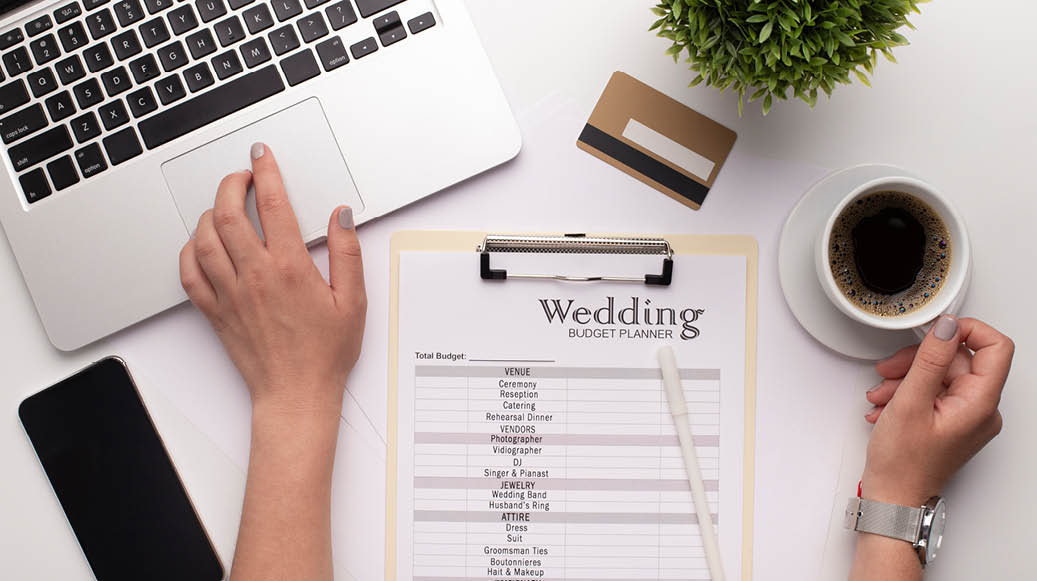 Wedding consultant constituting wedding plans and budget with laptop and smartphone, modern workplace