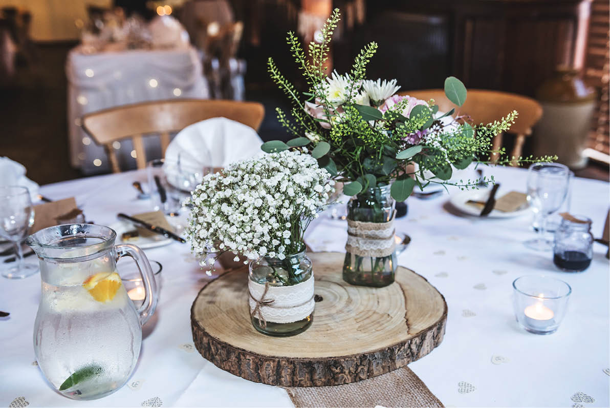 Wedding flowers displayed on a wooden log in the centre of a table at a wedding reception