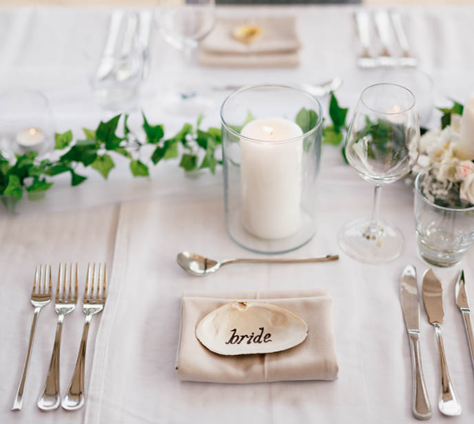 Close-up of a wedding dinner table. The inscription BRIDE on the shell in center of the table. Serving a table - knives, forks, glasses, wine glasses, candles, against background of gray tablecloth
