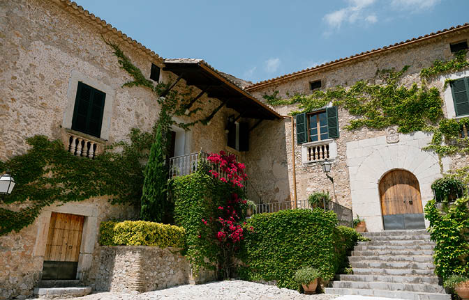A large stone building with a red roof and greenery around it. Description generated by AI