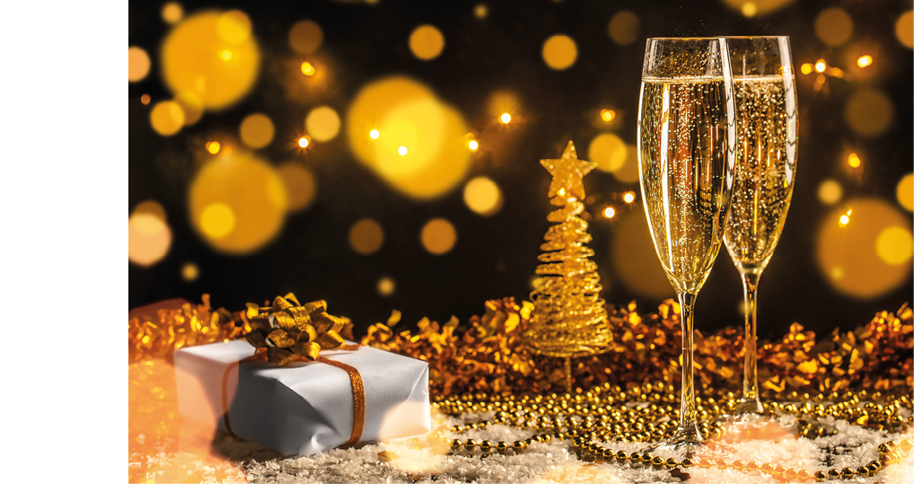 A glass of champagne is on a table with a Christmas tree and a gift. Description generated by AI