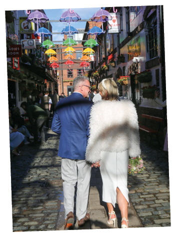 A man and woman walking down a street with colorful umbrellas above them. Description generated by AI