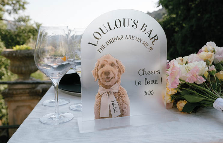 A small white dog figurine is sitting on a table next to a wine glass. Description generated by AI