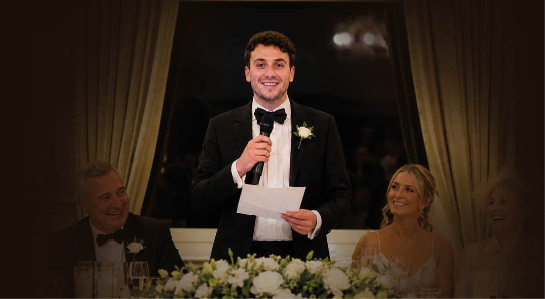 A man in a tuxedo is standing at a podium. Description generated by AI