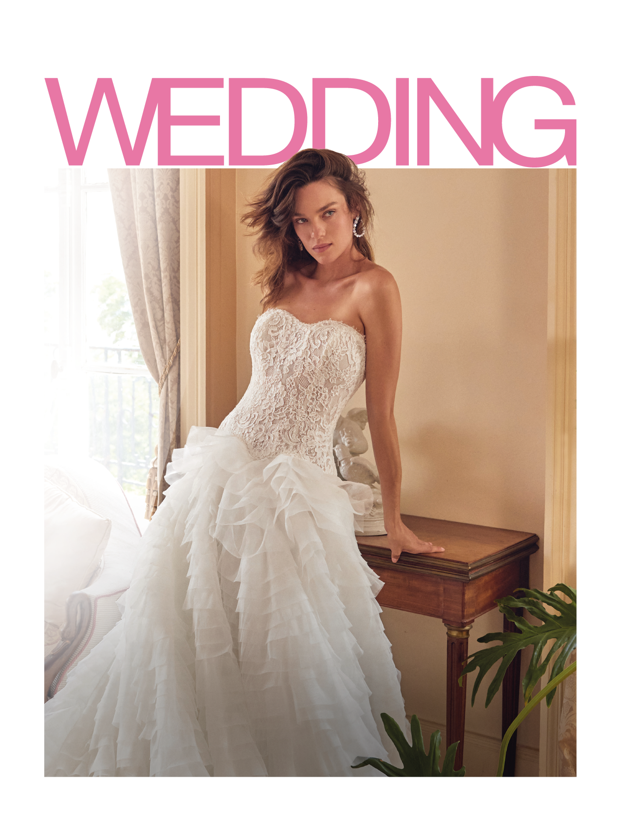 A person with wavy hair is wearing a strapless white wedding dress with a lace bodice and a voluminous ruffled skirt while leaning on a wooden table in a softly lit room. Description generated by AI