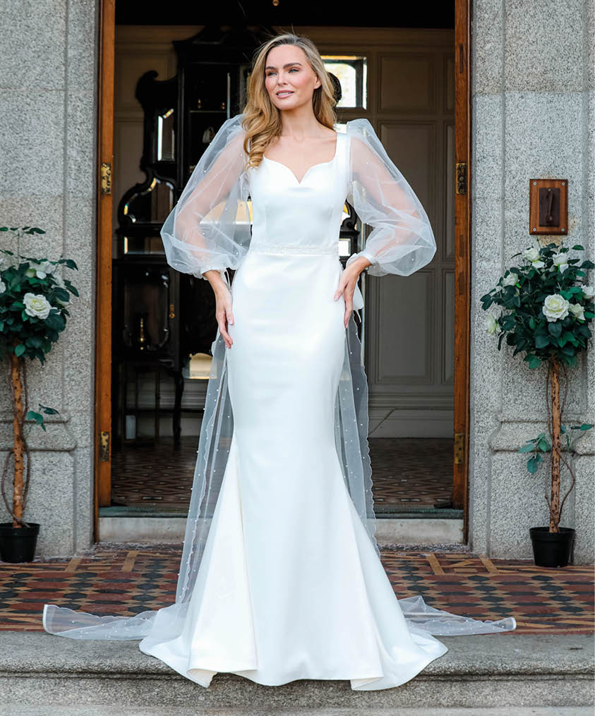A woman in a white dress standing in front of a doorway. Description generated by AI