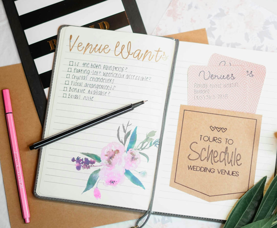 A notebook with a pink pen and a note that says “venue wanted" on it. Description generated by AI