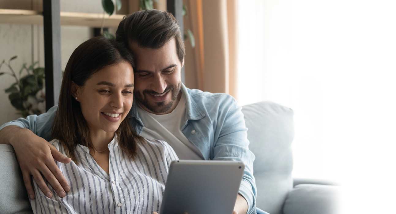 A man and woman sitting on a couch, the woman holding a tablet. Description generated by AI
