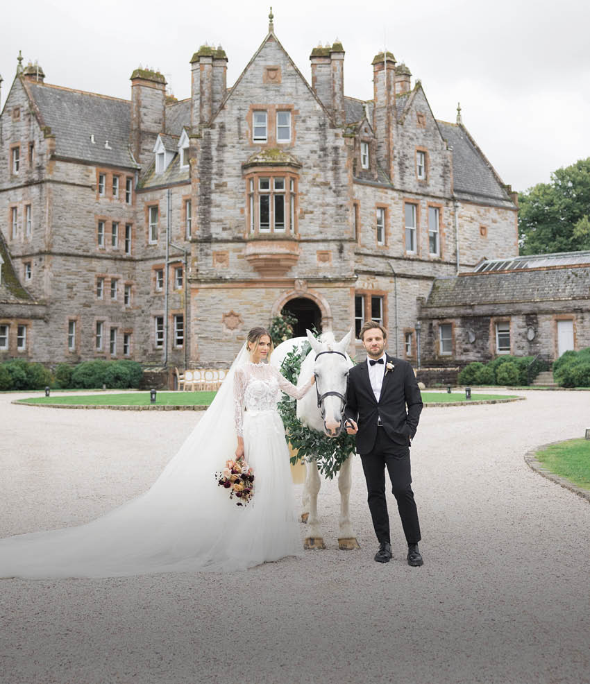 A bride and groom standing in front of a large building. Description generated by AI