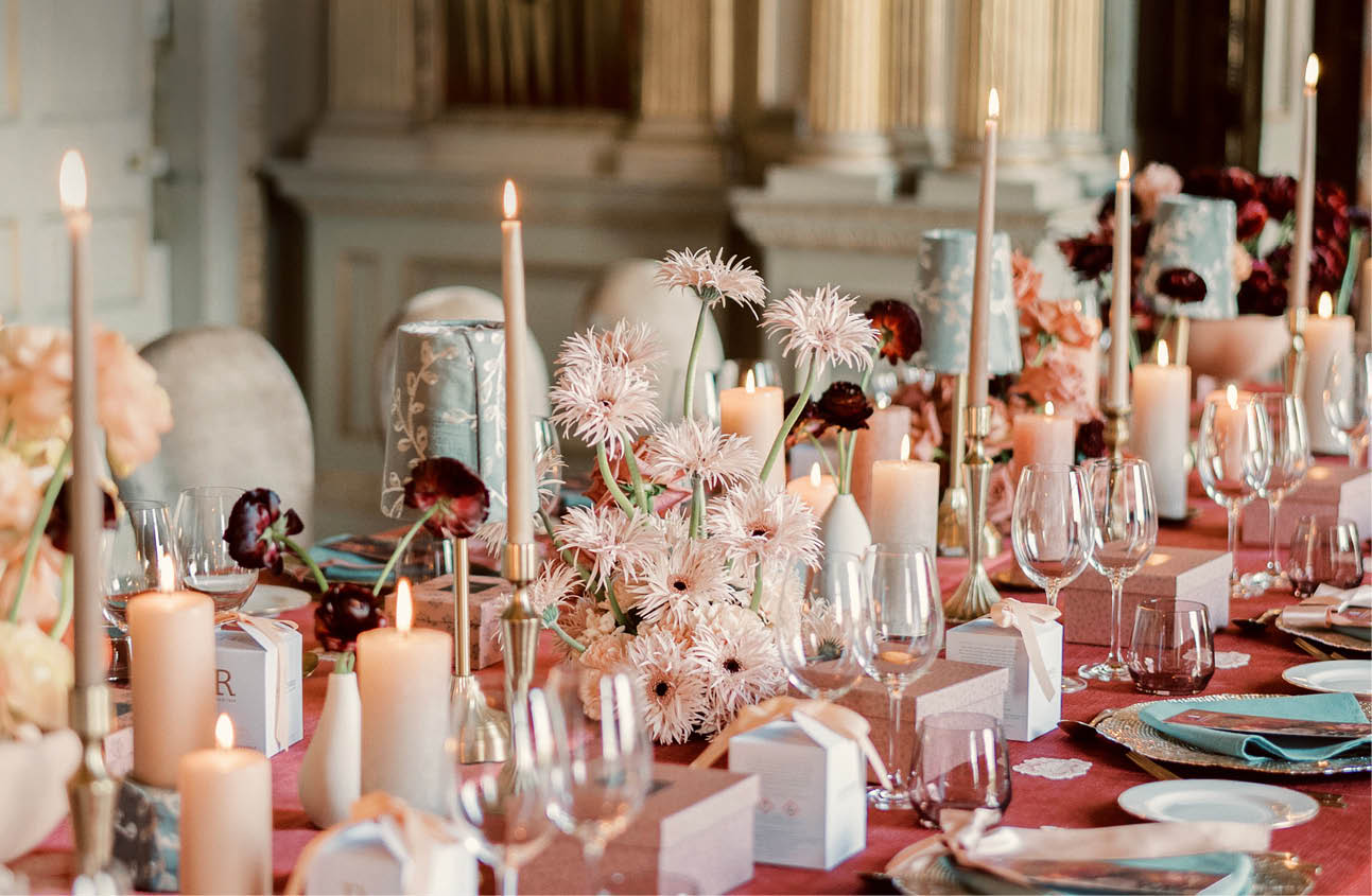 A long red table with a white tablecloth and place settings. Description generated by AI