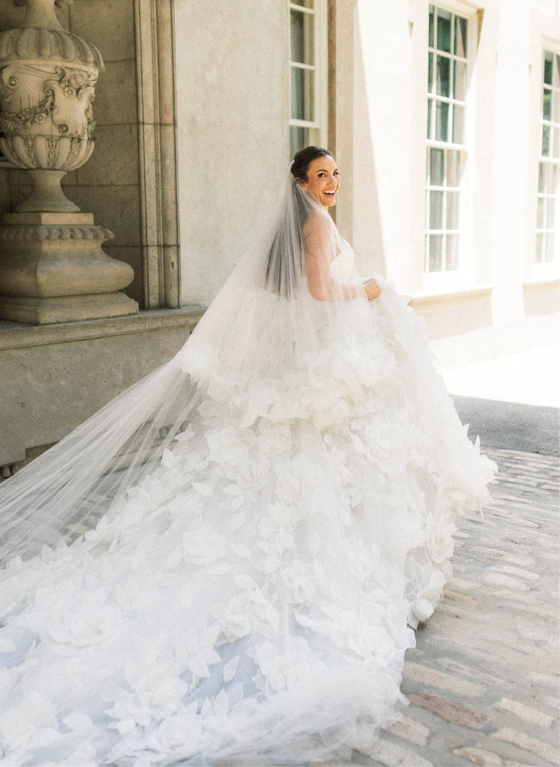 A woman in a white dress with a veil standing in front of a building. Description generated by AI
