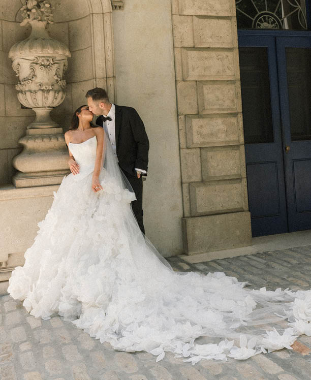 A bride and groom standing in front of a building. Description generated by AI
