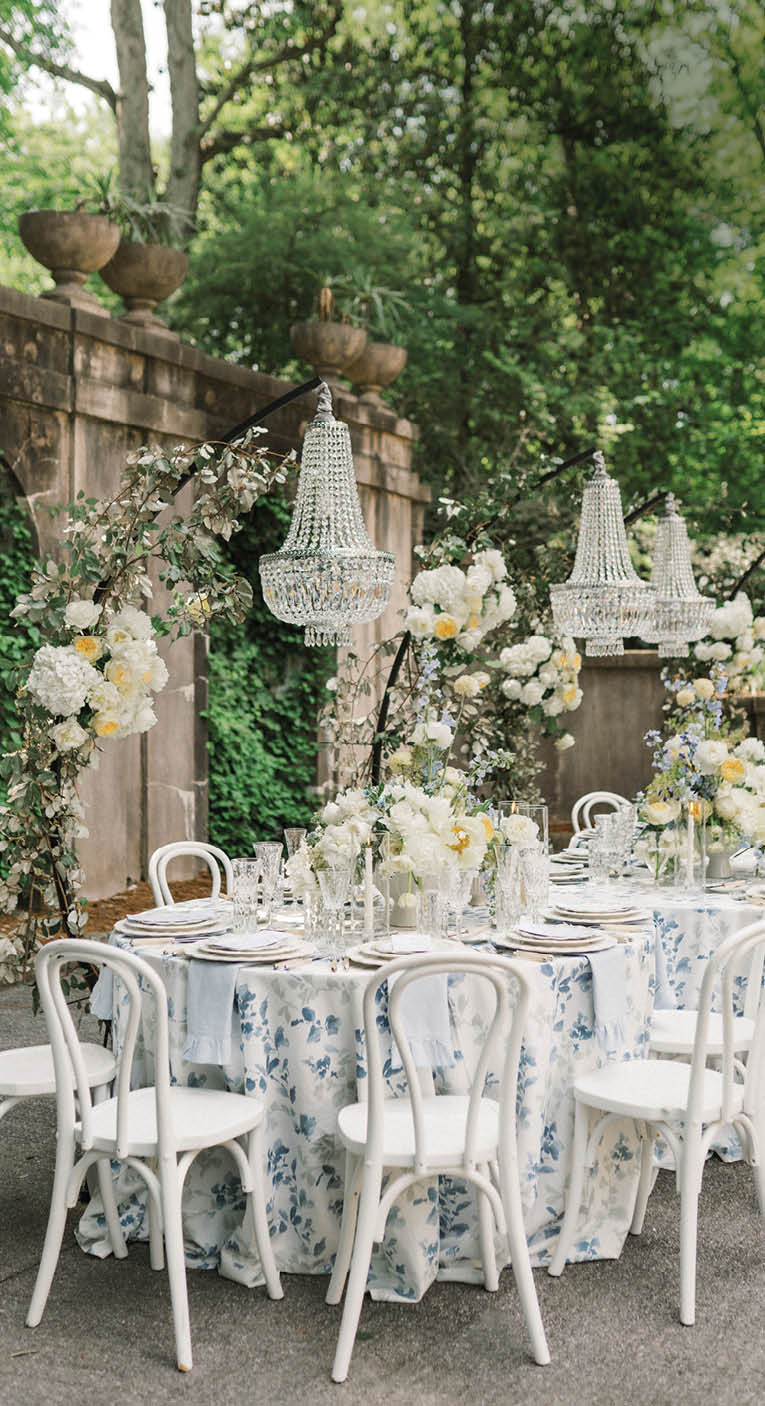 A table with a blue and white tablecloth and white chairs. Description generated by AI