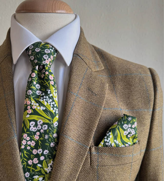 A brown suit jacket with a green and white flower tie. Description generated by AI