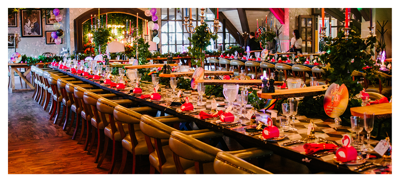 A long dining table with chairs and a red tablecloth. Description generated by AI