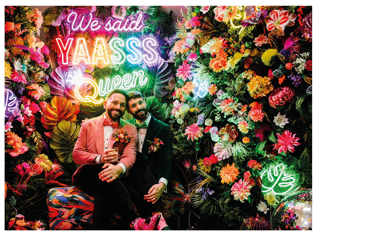 Two men sitting in front of a wall with pink and green neon lights. Description generated by AI