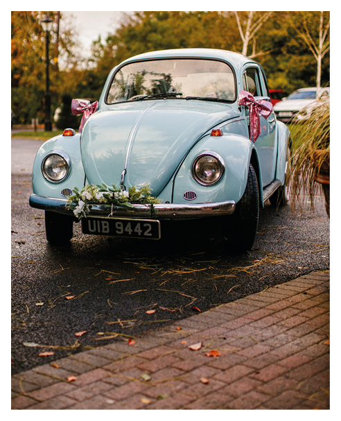A blue Volkswagen Beetle with a floral arrangement on the hood. Description generated by AI