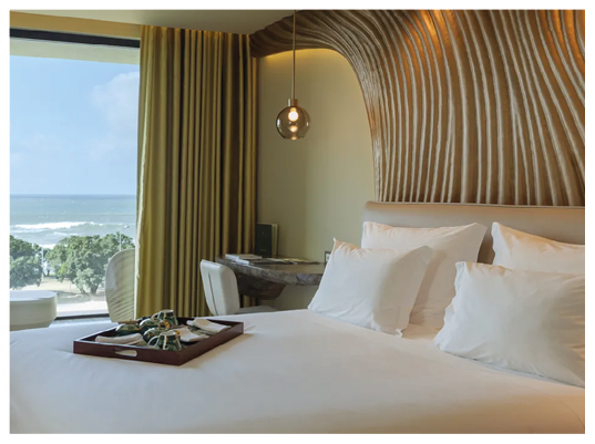 A bed with white pillows and a view of the ocean. Description generated by AI