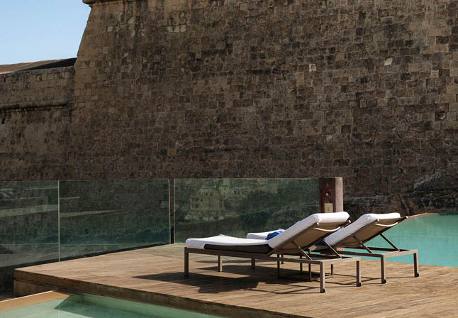 A lounge chair is on a deck overlooking a pool. Description generated by AI