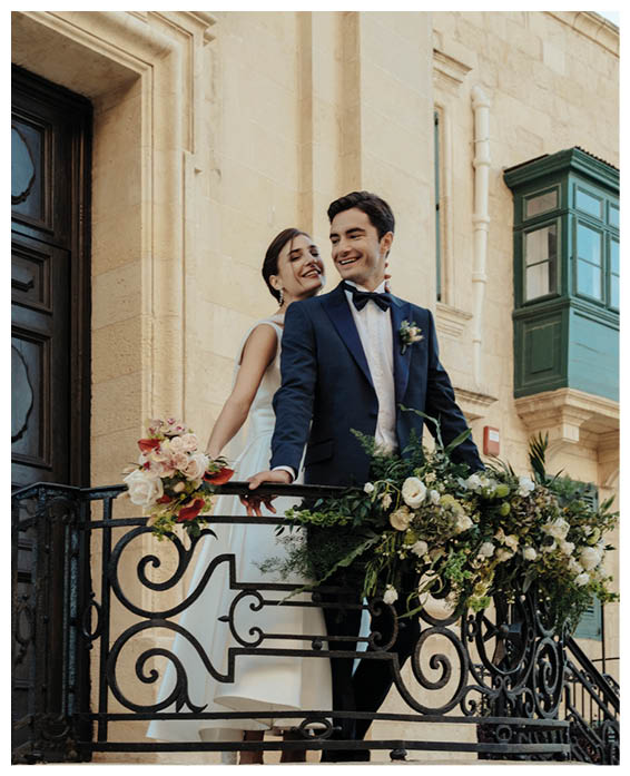 A man and woman standing on a balcony with flowers. Description generated by AI