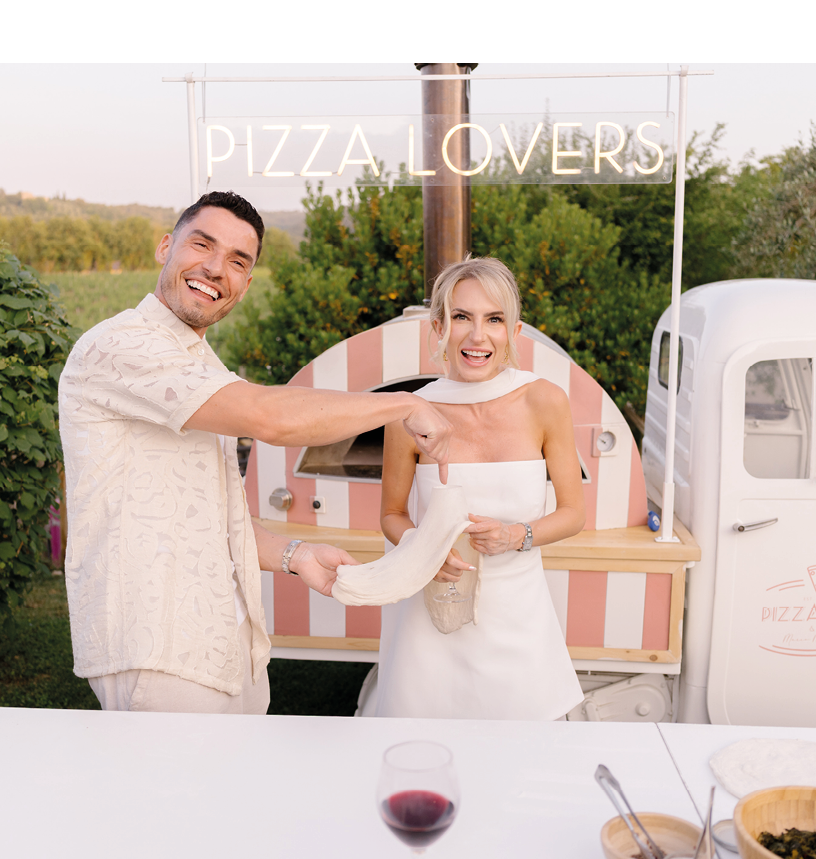 A man and a woman are standing in front of a pizza oven. Description generated by AI