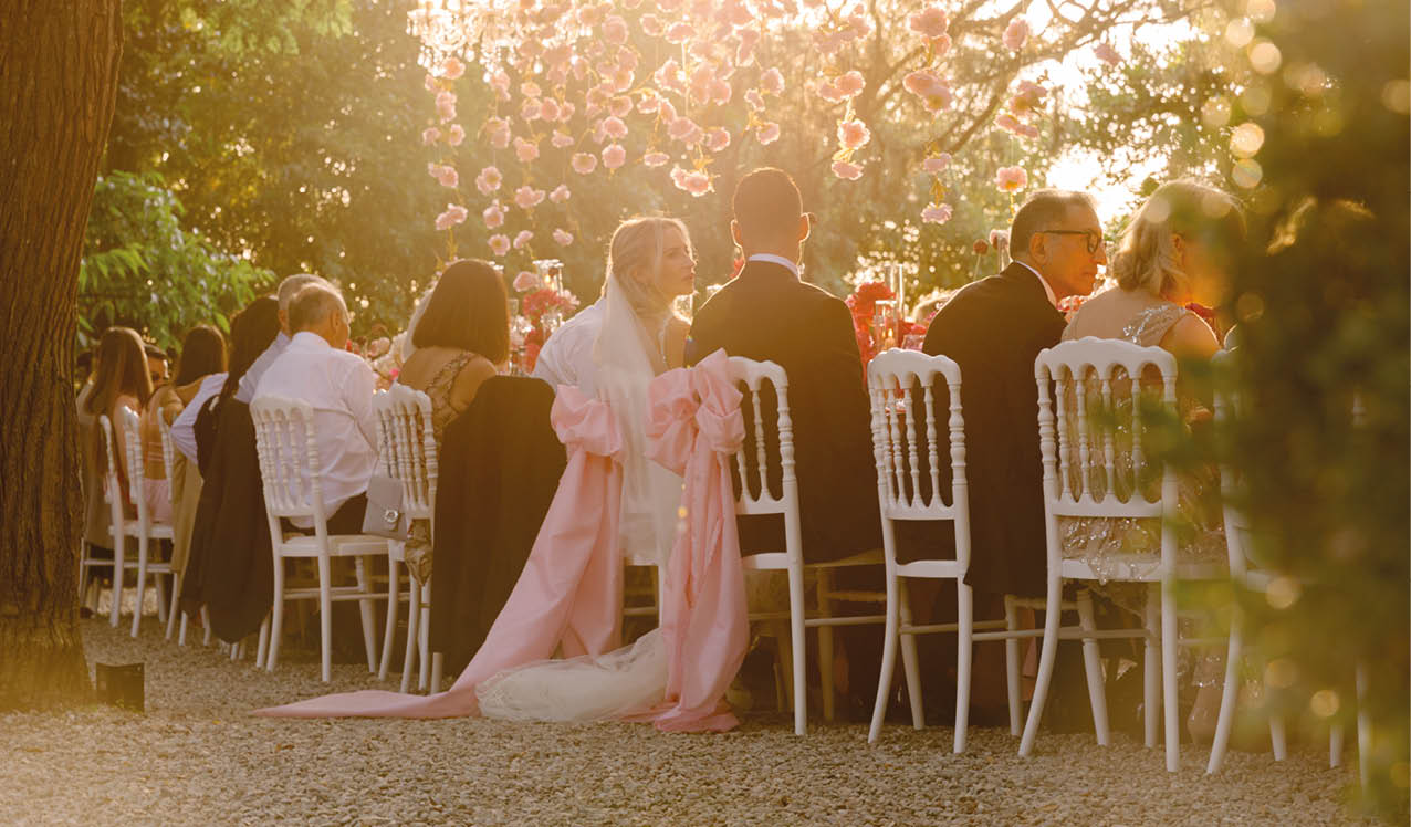 A bride and groom sit at a table with other guests. Description generated by AI