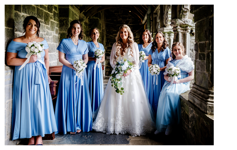 A group of women wearing blue dresses and holding flowers. Description generated by AI