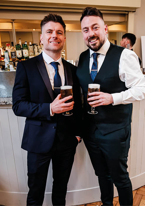Two men in suits and ties holding beers. Description generated by AI