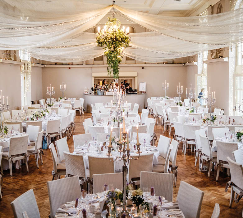 A large room with a long table set for a wedding reception. Description generated by AI