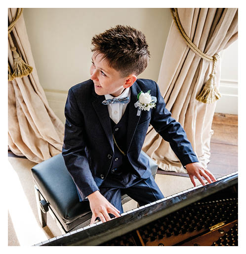A boy in a suit is playing a piano. Description generated by AI