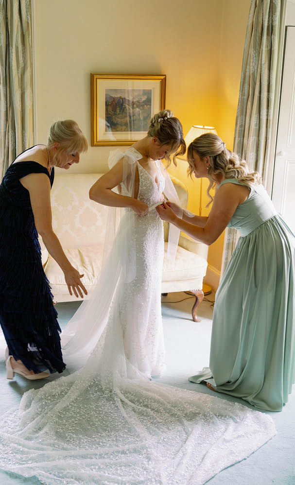 Three women are helping a bride with her wedding dress. Description generated by AI
