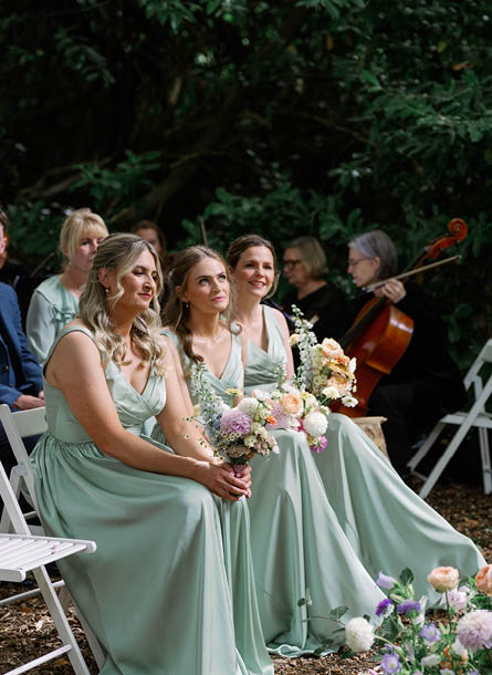 Three women in green dresses sitting on chairs. Description generated by AI