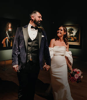 A bride and groom standing in front of a building. Description generated by AI