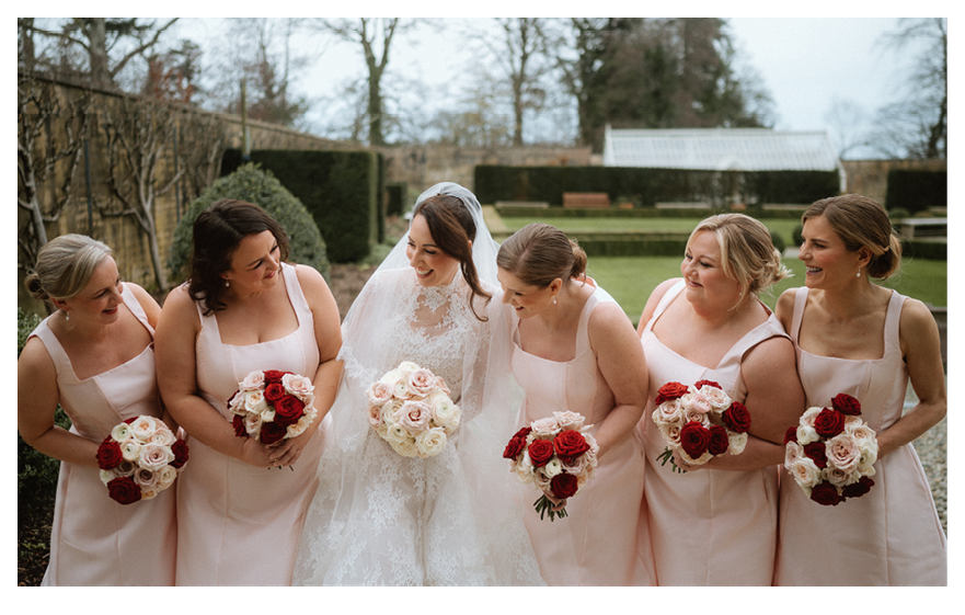 Five bridesmaids wearing pink dresses and holding bouquets of red and white flowers. Description generated by AI