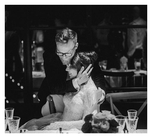A man and woman sitting at a table with a bouquet of flowers in front of them. Description generated by AI