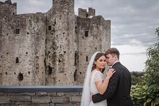 A bride and groom standing in front of a castle. Description generated by AI