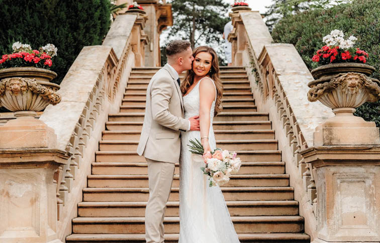 A bride and groom standing on a set of stairs. Description generated by AI