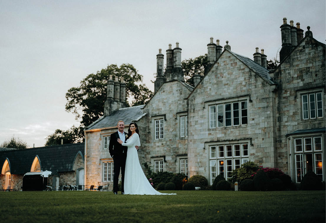 A bride and groom standing in front of a large building. Description generated by AI