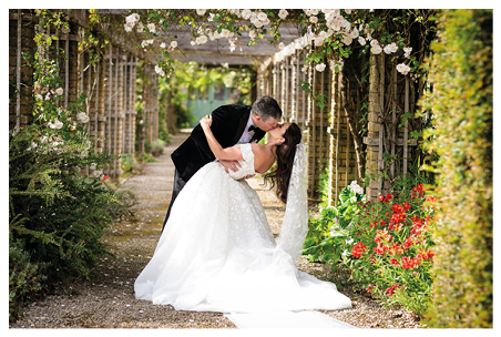 A bride and groom standing in front of a large building. Description generated by AI