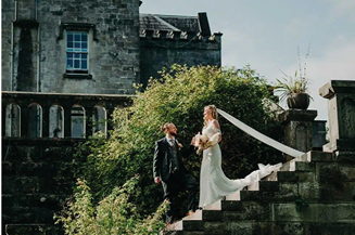 A bride and groom are standing on a set of stairs in front of a castle. Description generated by AI