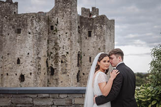 A bride and groom standing in front of a castle. Description generated by AI